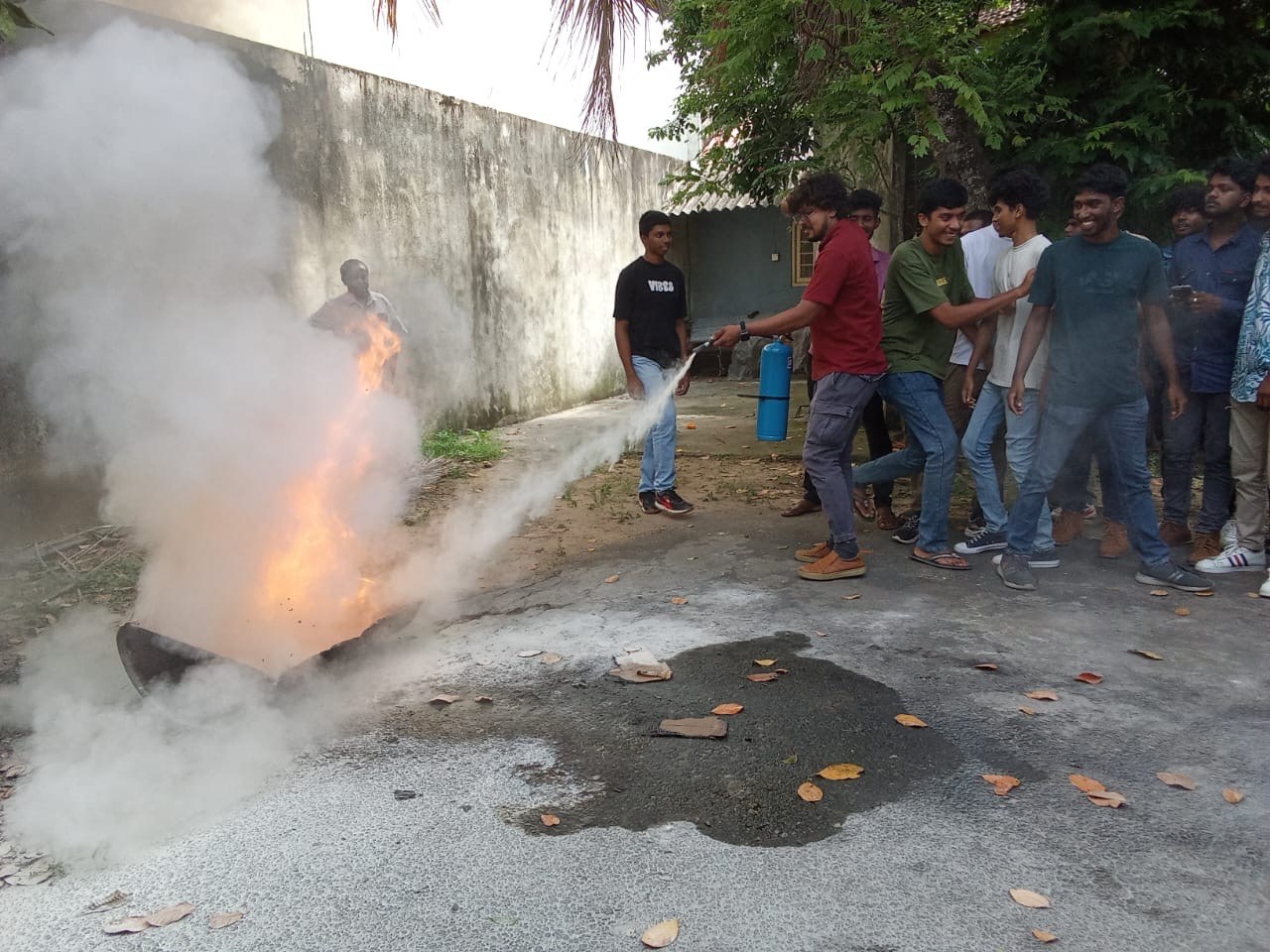 Factory trainee practicing chemical powder discharge onto open flame pit under supervision